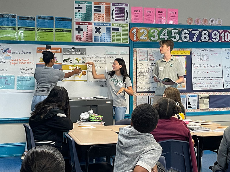 Three Freeman School students point to a classroom whiteboard while elementary students look on. 