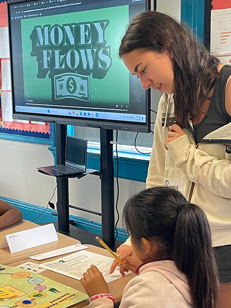 A Freeman college student looks over the shoulder of a young girl at a desk.