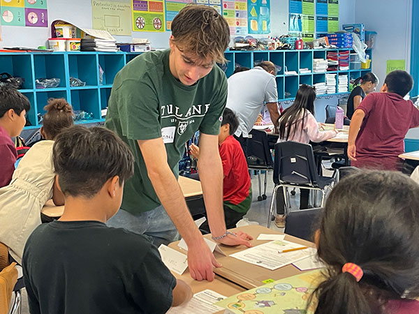 A Freeman college student looks on as elementary school students work at a desk. 