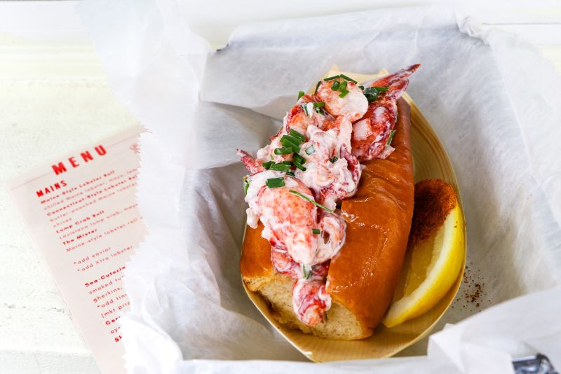 A lobster roll beside a Nell Shell menu. 