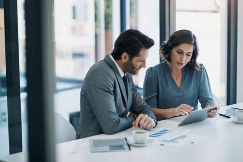 Two business analysts review data on a tablet in an office.