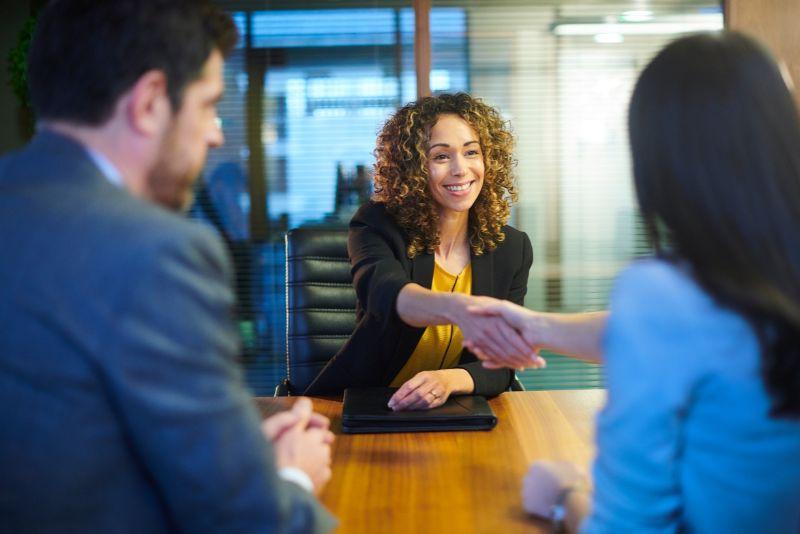 A professional MBA graduate shakes hands at a job interview.