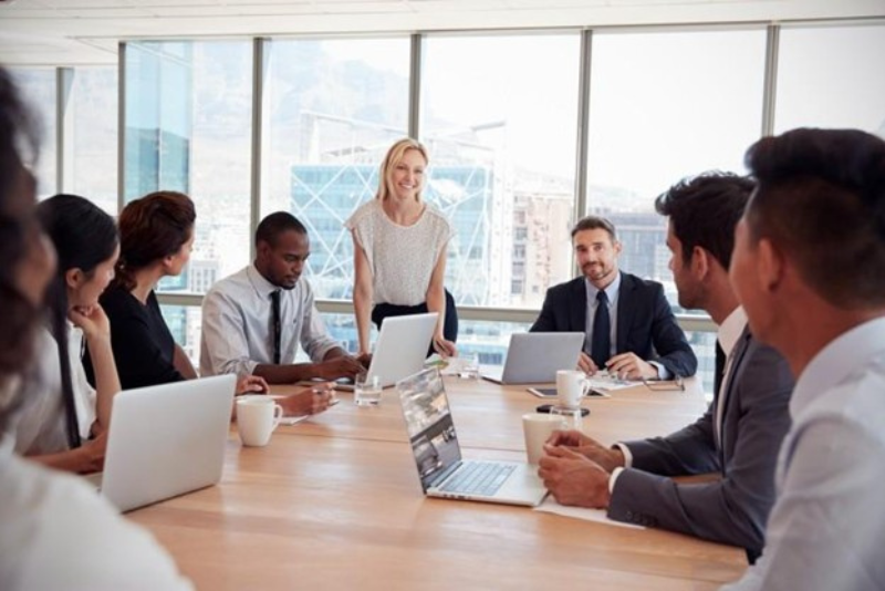 A sales manager leads a team meeting around a conference table.
