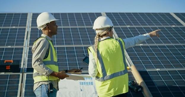 A sustainability manager and a contractor, both wearing hardhats and reflective vests, review a solar array.