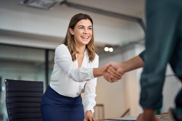 A bank branch manager shakes hands with a client over a desk.