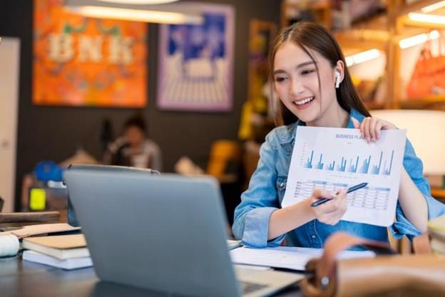 A Master of Business Analytics student holds up a business plan document during an online business analytics course.