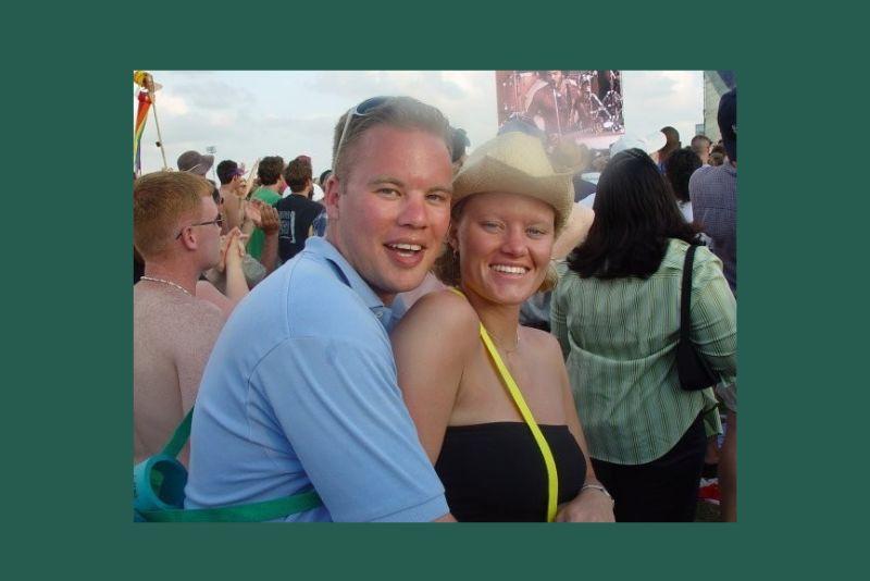 Smiling man with arm around woman in cowboy hat, both happy in a crowd.