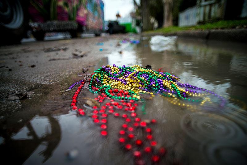 Discarded Mardi gras beads lie on a muddy, wet street