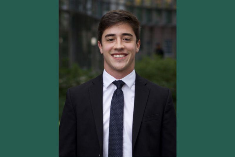 Professional headshot of a smiling young man in a black suit.