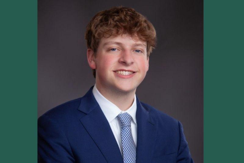 Young man with curly brown hair in blue suit and tie smiling.