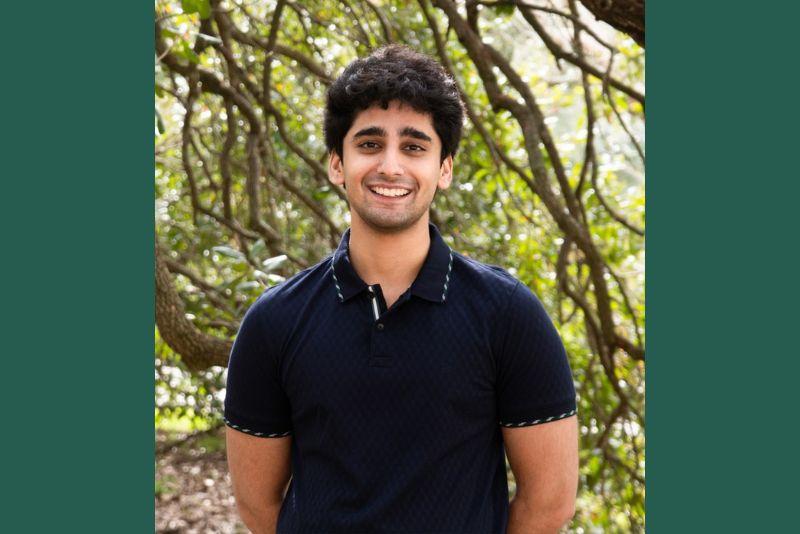 Smiling young man with dark, curly hair in a navy polo shirt outdoors.