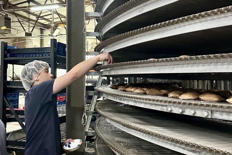 Worker in hairnet inspects items on a spiral industrial food rack.