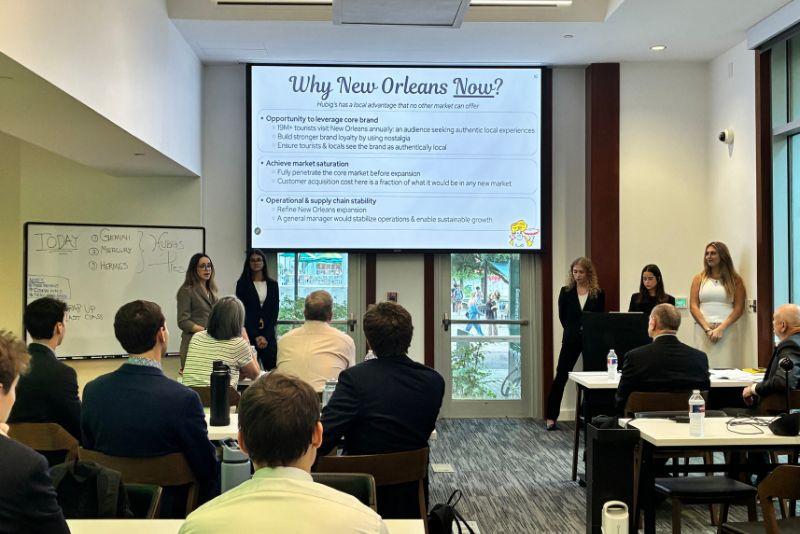 Students present a business proposal to an audience in a bright classroom.
