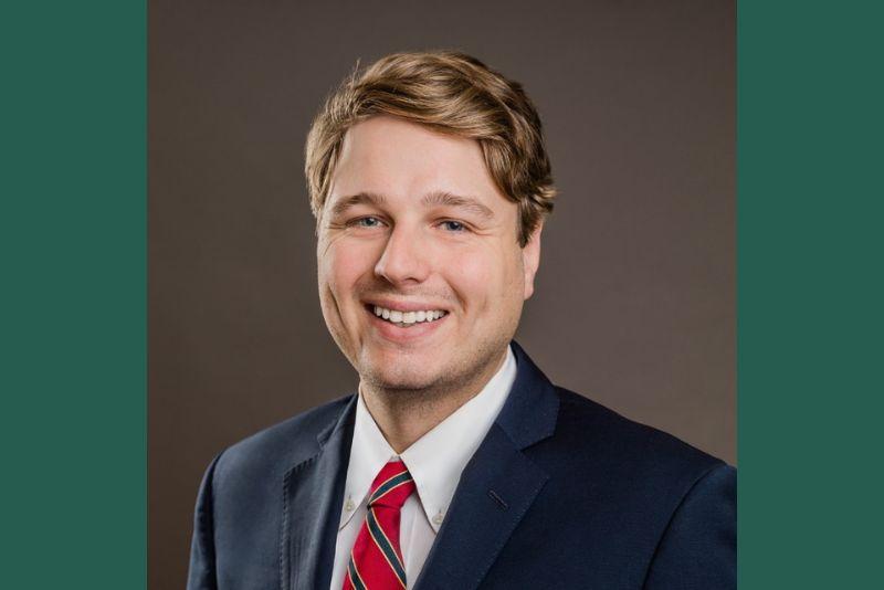 Professional headshot of a smiling man in a dark suit and red tie