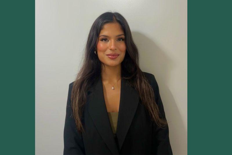 Smiling woman with long dark hair, black blazer, and a delicate pearl necklace.