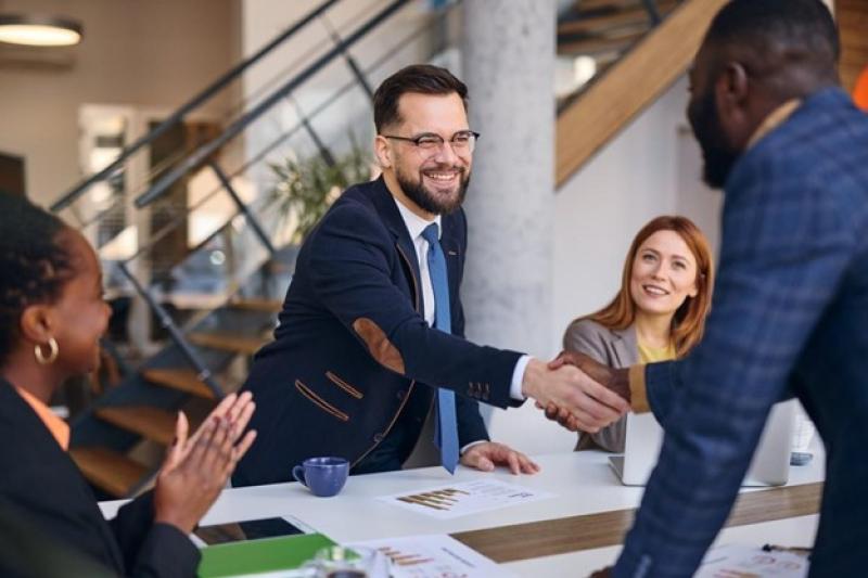Two businesspeople at a conference table shake hands after a successful negotiation.