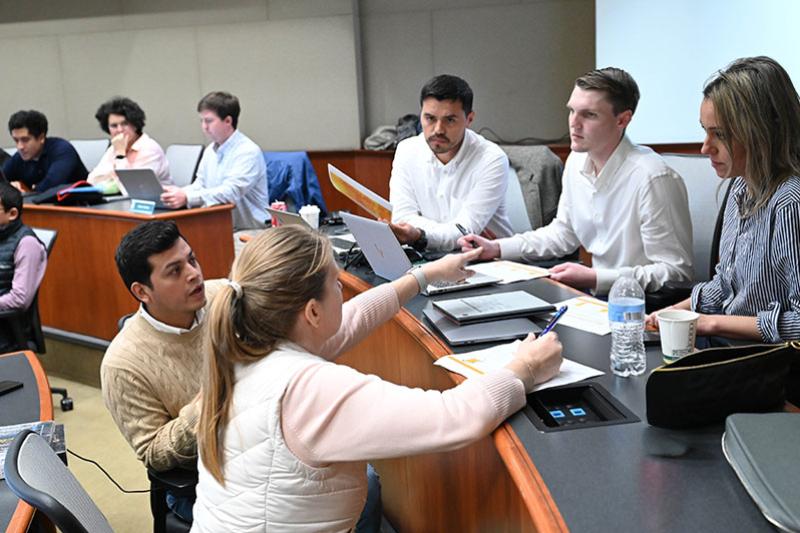 Students in a classroom actively discussing, with one woman pointing at a document.