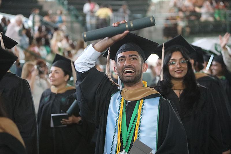 Excited graduate in cap and gown holds diploma overhead at ceremony.