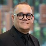 Professional man in black suit, black shirt, and black-rimmed glasses.