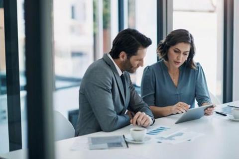 Two business analysts review data on a tablet in an office.