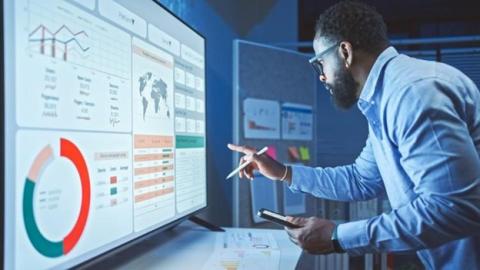 A business analyst reviews a data dashboard on a smartboard