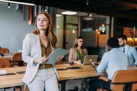 A business executive standing in an office while co-workers meet in the background.