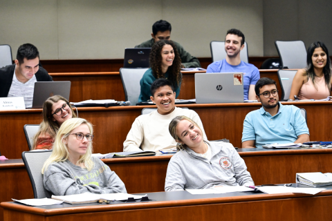 MBA students sit and take notes in a lecture hall. 
