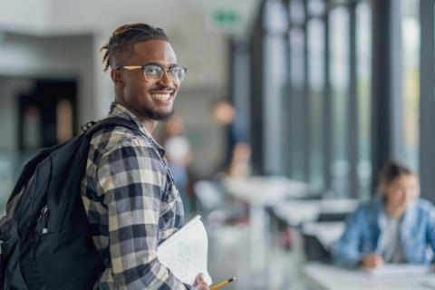 A smiling MBA student wearing a backpack and holding a notebook.