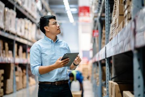 A retail manager holds a tablet and checks inventory in a warehouse.