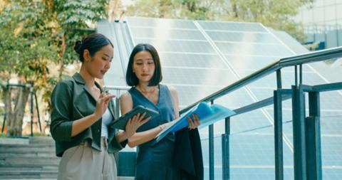 Two renewable energy consultants look at a tablet and documents next to a solar panel.