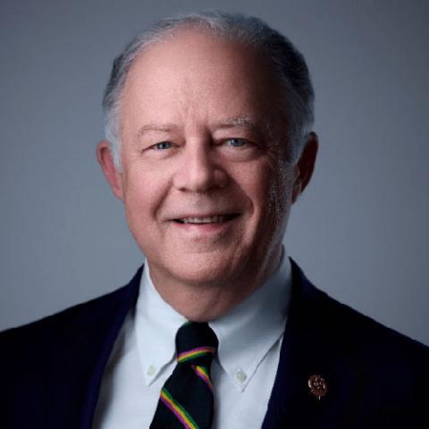 Smiling man with grey hair, blue eyes, dark suit, and striped tie.