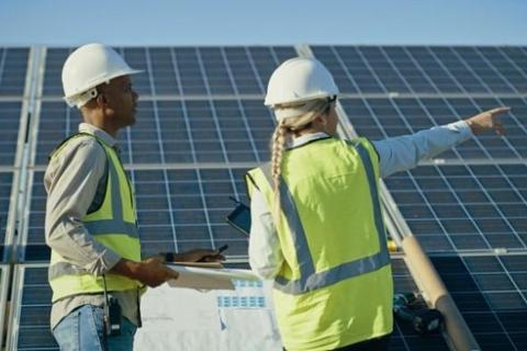 A sustainability manager and a contractor, both wearing hardhats and reflective vests, review a solar array.