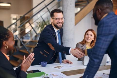 Two businesspeople at a conference table shake hands after a successful negotiation.