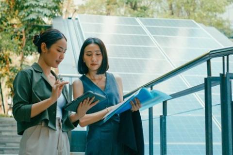 Two renewable energy consultants look at a tablet and documents next to a solar panel.