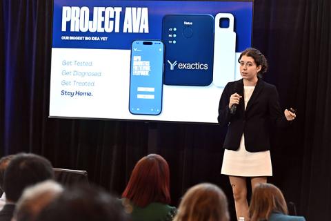 Woman presents "Project AVA" on a screen showing a mobile app and exactics device to an audience.