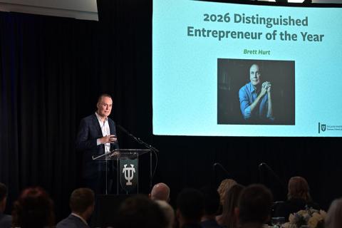 Man speaking at podium. Screen announces '2026 Distinguished Entrepreneur of the Year Brett Hurt' with photo.