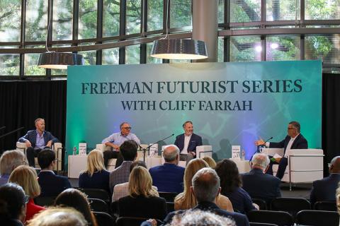 Four speakers sit in chairs on a stage in front of a backdrop that says Freeman Futurist Series with Cliff Farrah