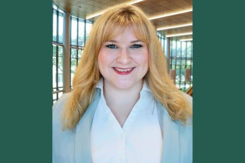 Blonde woman with bangs and blue eyes smiling in a white shirt and light blue blazer.