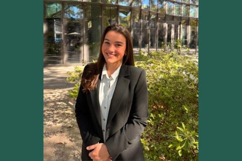 Smiling woman in black blazer and white shirt outdoors in front of a modern building.