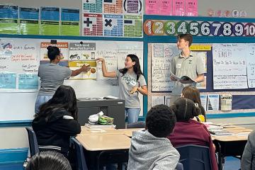 Three Freeman School students point to a classroom whiteboard while elementary students look on. 